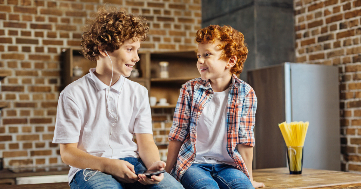 Two red-headed boys sitting on the counter i n the kitchen smiling because they're lice free.
