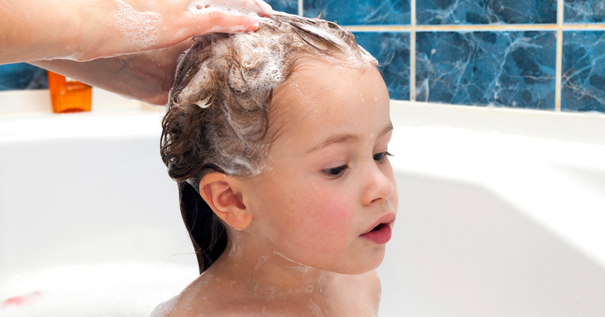 A little girl in the bathtub with her mom washing her hair with natural lice shampoo.