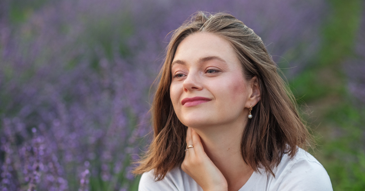 A woman sitting in a lavender field smiling because her natural head lice treatment worked.