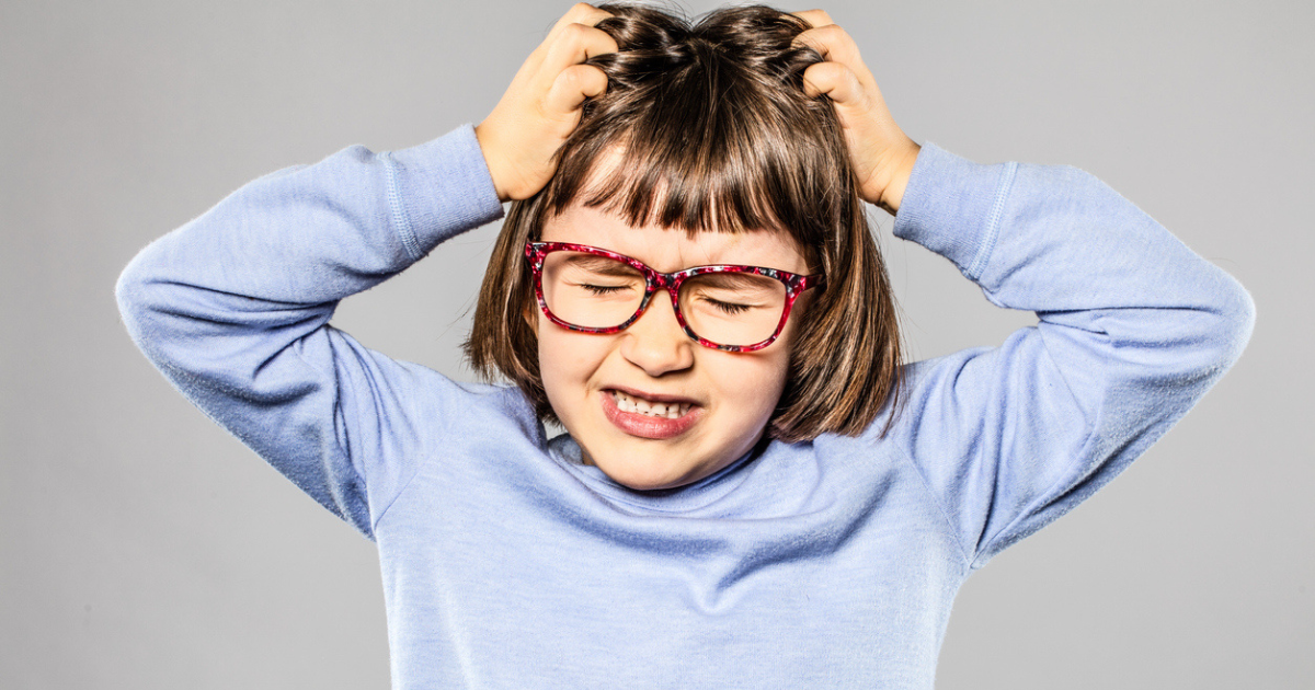 A little girl with glasses scratching her head because it itches from lice.
