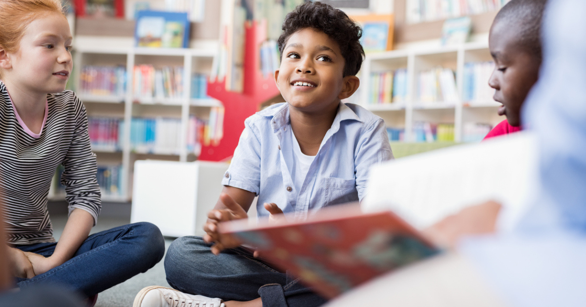 A little boy sitting on the floor at his school during story time.