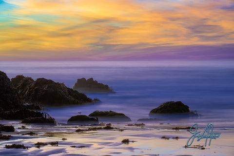 Serene sunset over Big Sur with smooth purple sand leading to calm waters, reflecting a tapestry of vibrant skies