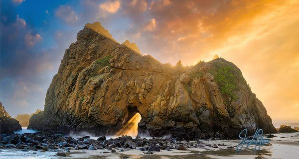 The majestic Keyhole Arch in Big Sur stands against a sunset, its silhouette framed by a golden sky, embodying the timeless allure of California's rugged coastline as the sun shines the keyhole in the rock.