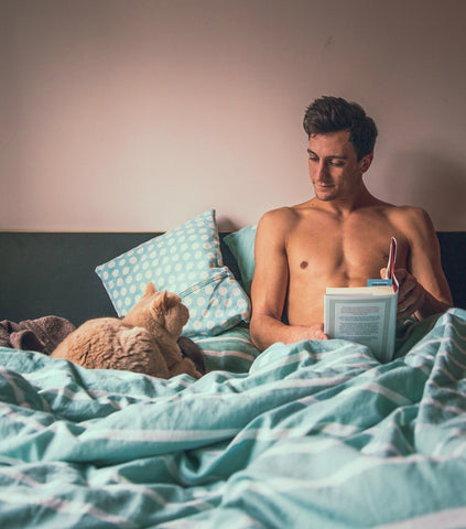 man in bed with cat reading book