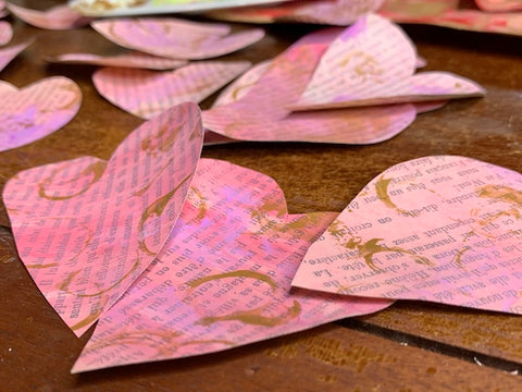 old book pages painted pink and gold then cut into heart shapes to make homemade Valentine's Day cards