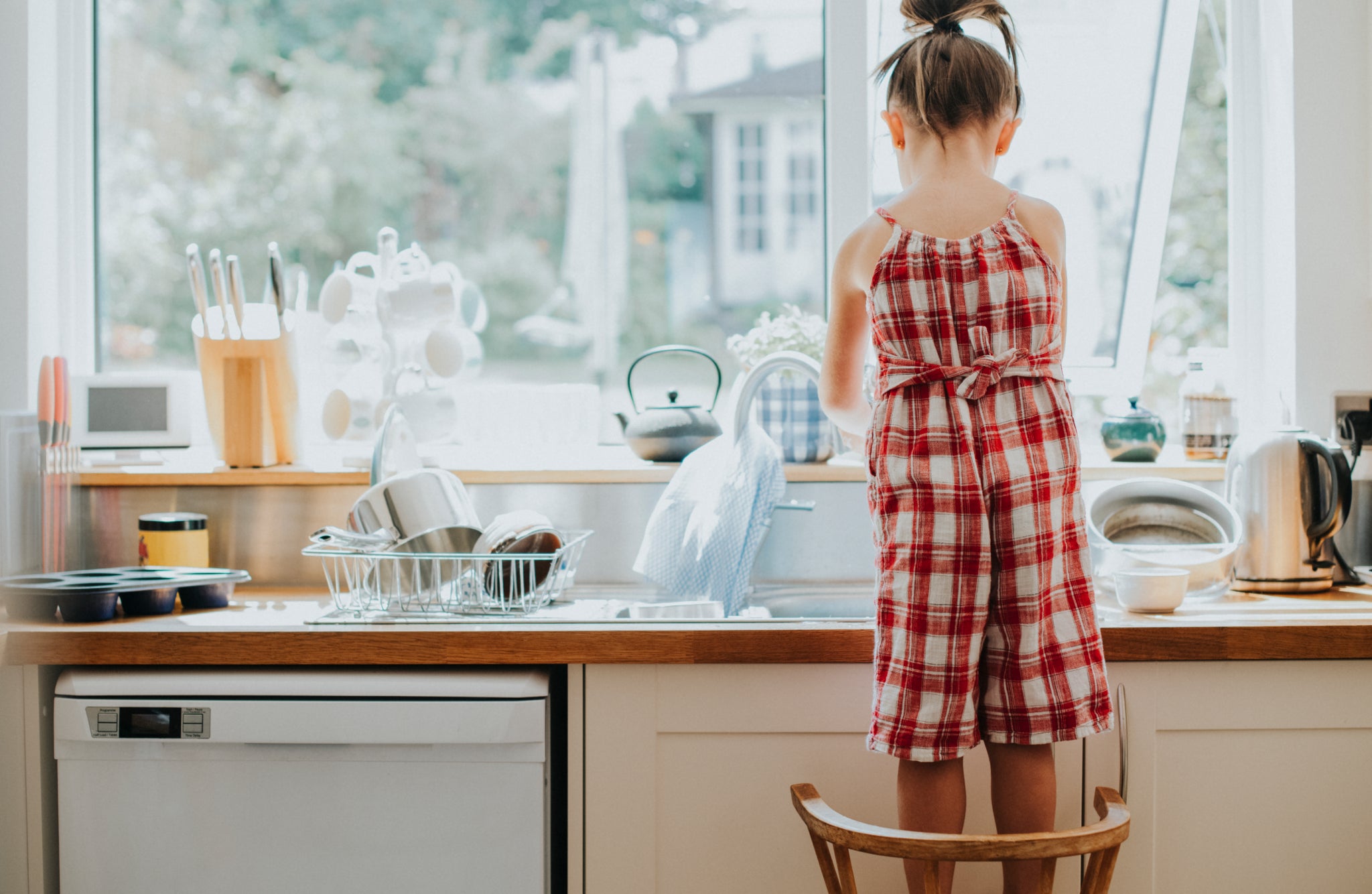 A child washing dishes under warm windows light