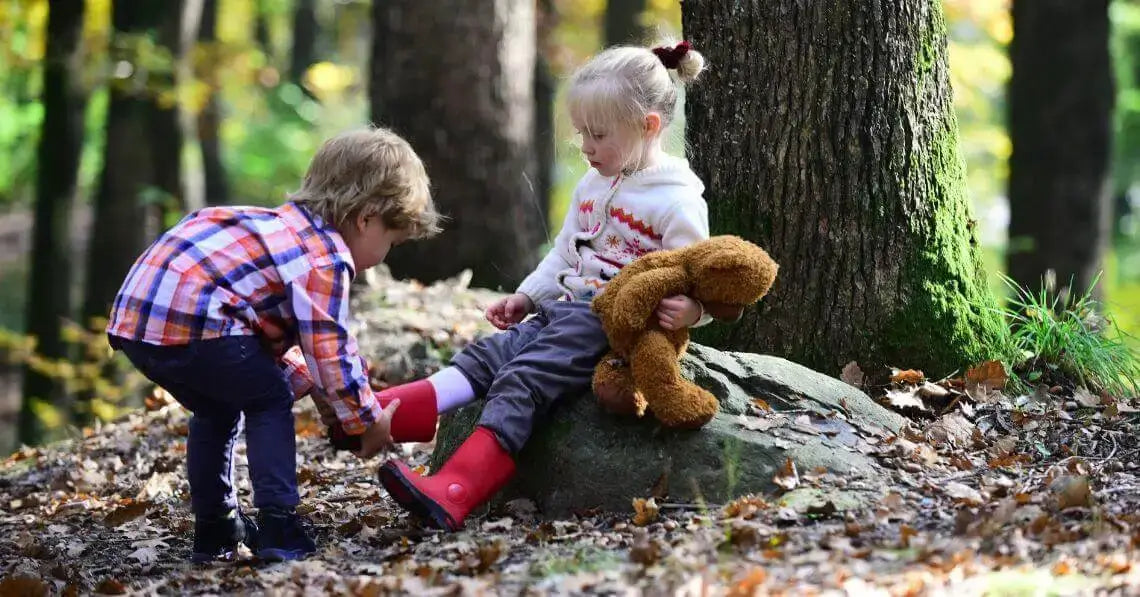 A toddler boy helping a toddler girl with her boots