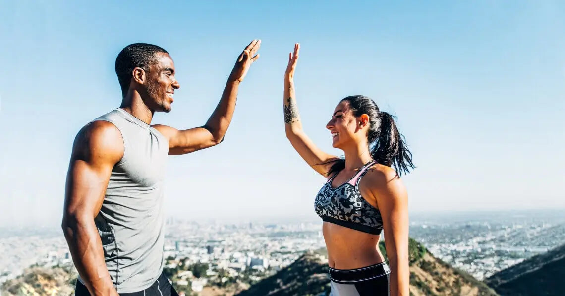 a couple of athletic friends high-fiving on top of a hill