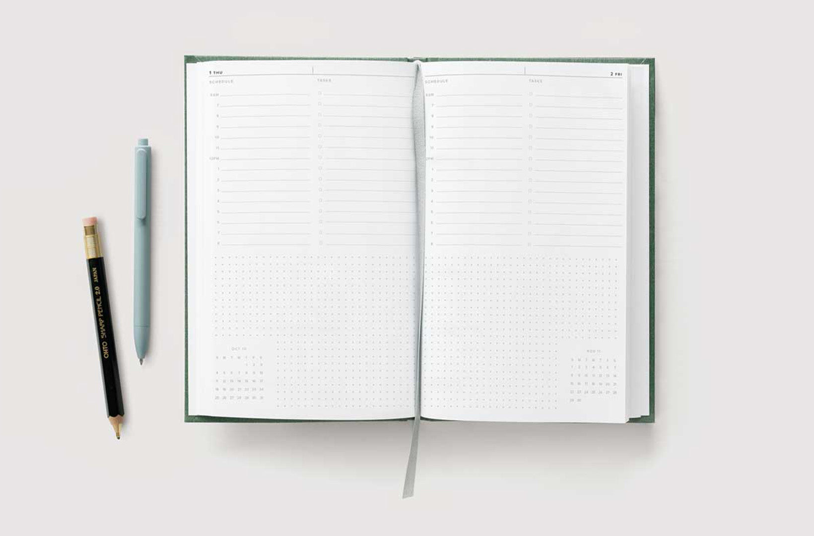 A 23-24 Hardcover Daily Planner lies open against a light gray background. Two writing tools sit aside.