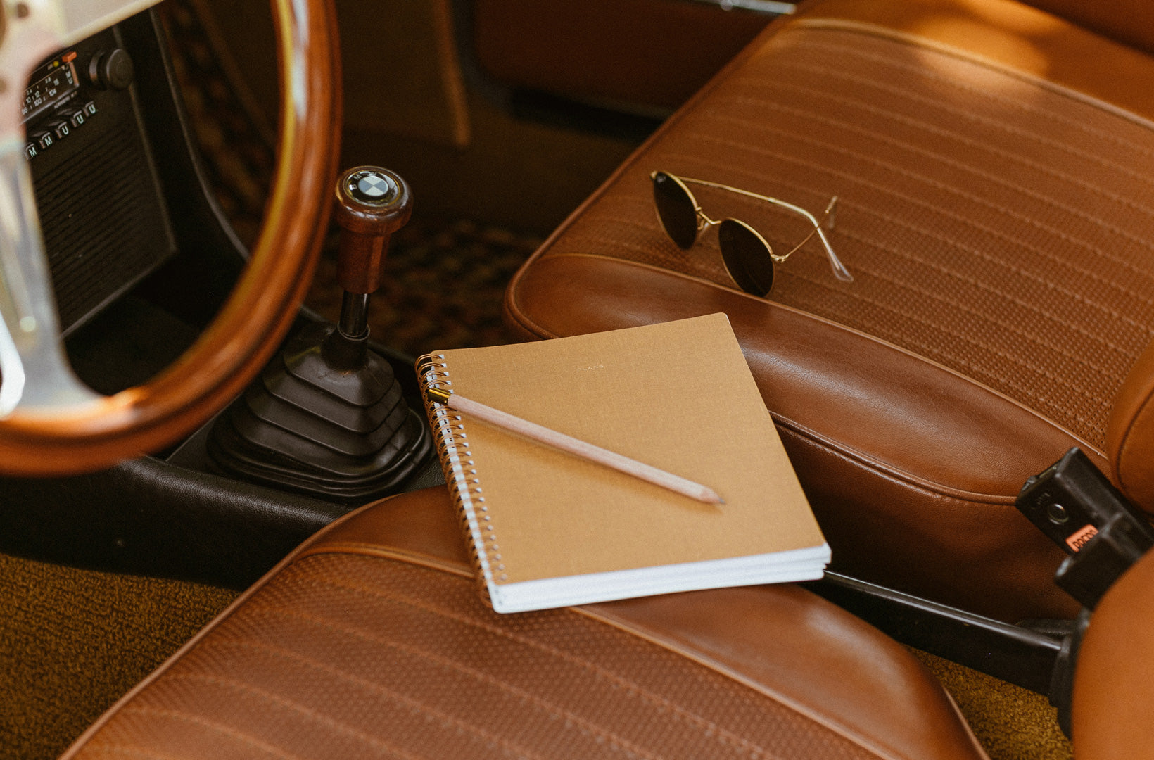 The Appointed Vision Journal, a light brown bookcloth journal with brass binding, sits on the front set of a cart with brown leather seats and a leather steering wheel.