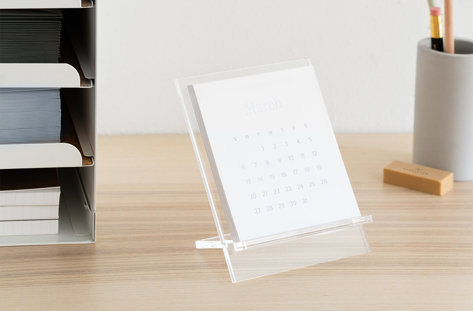 The 2022 Acrylic desk calendar sits atop a wood desk with other desk accessories including a pencil cup, erase, and file organizer