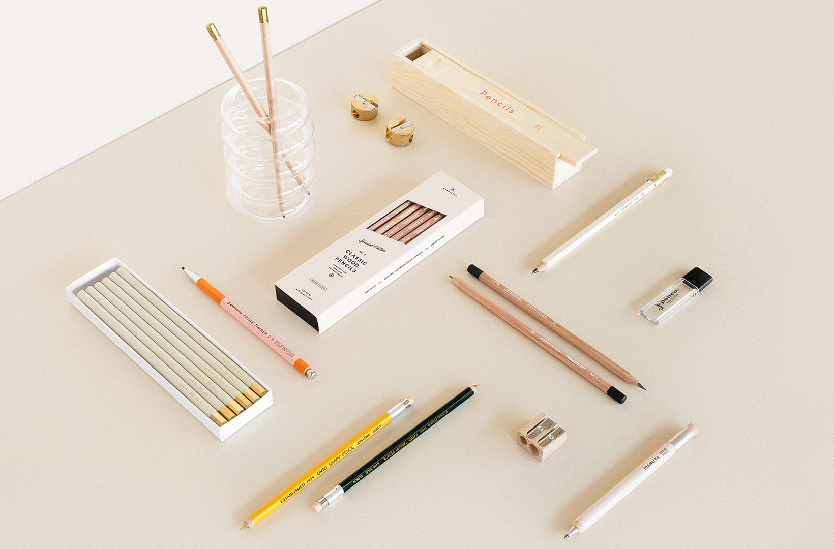 A selection of desk accessories and writing tools sit on a beige background, arranged perpendicular to each other in a pleasing way