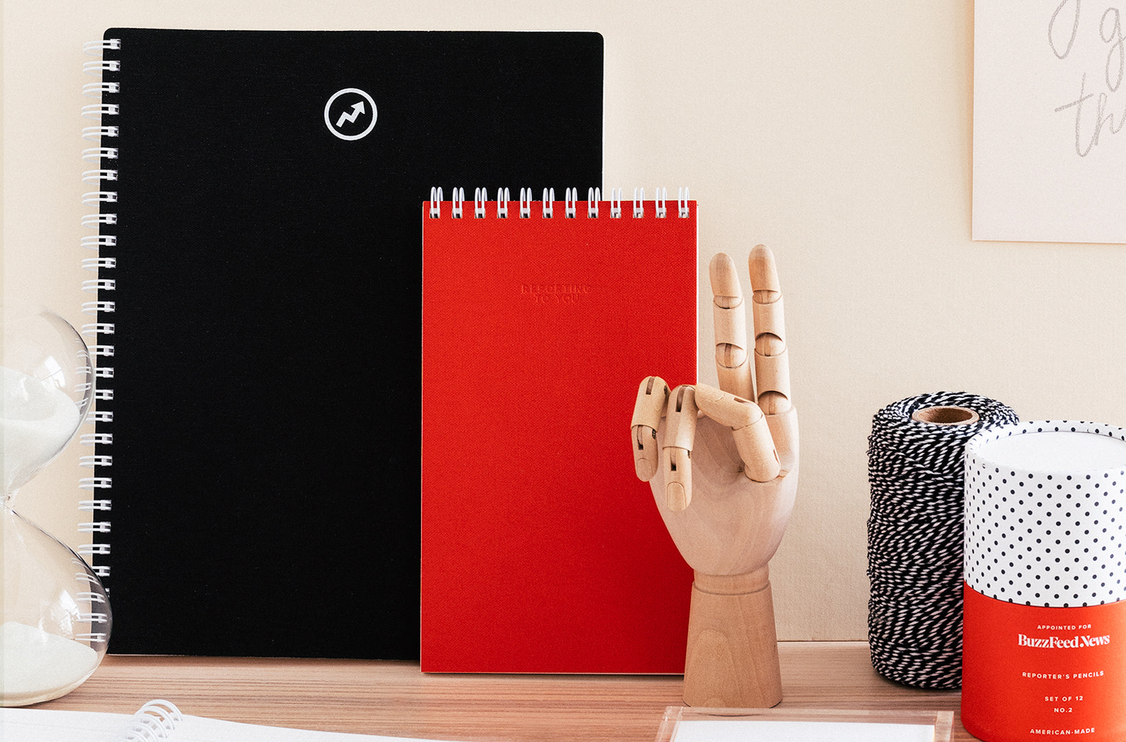 The Appointed for BuzzFeed News Notebook, Reporter's Notepad, and Pencil Set sit on a desk with a wood hand desk accessory making a peace sign.