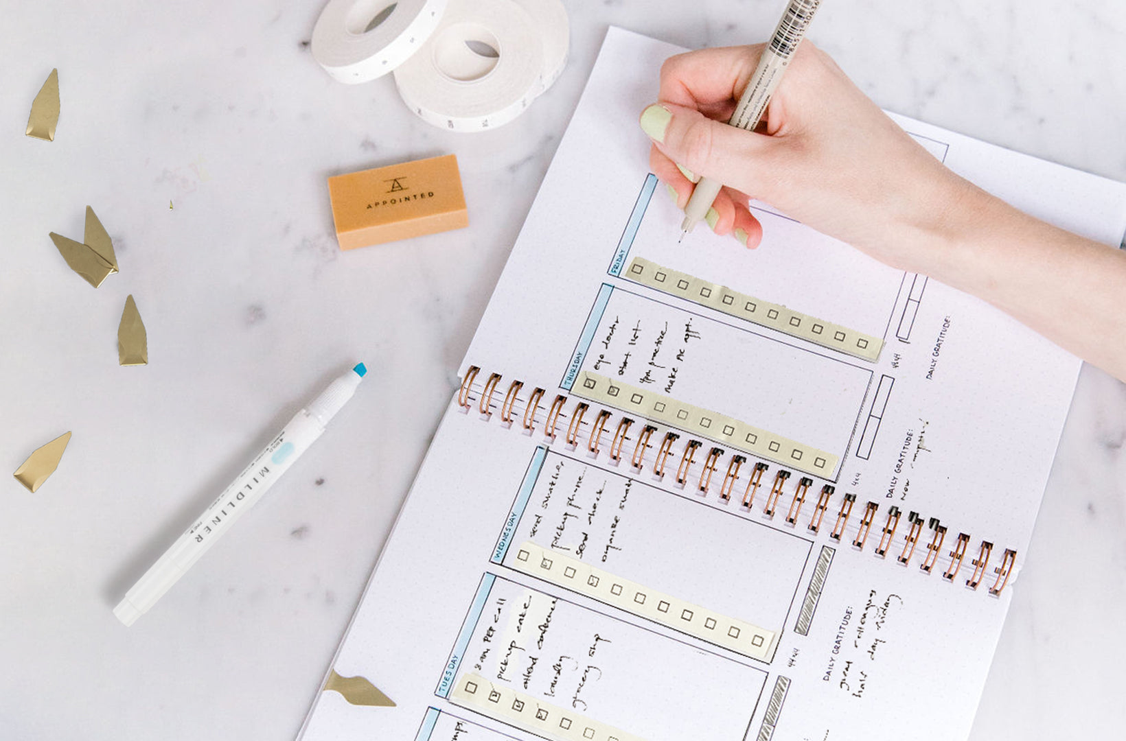 An Appointed workbook lies open on a marble desktop, showing a colorful summer bullet planning spread. Mildliner highlighters, brass page markers, and other accessories sit aside.
