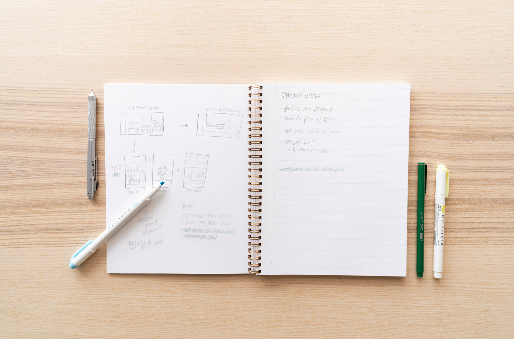 A notebook lies open to show hand-drawn lists & charts with various writing utensils alongside.