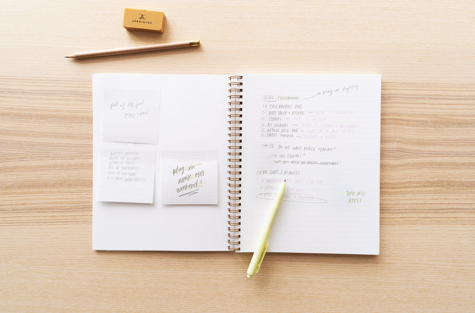 A notebook lies open on a wood desktop to show to do lists organized with adhesive notes and writing accessories alongside