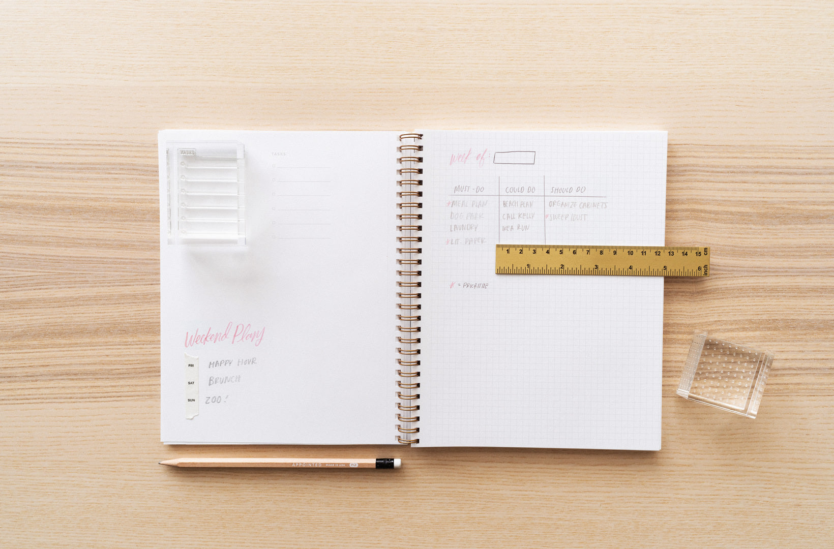 A notebook lies open on a wood desk with stamps, paper taper, and other stationery accessories laid across.