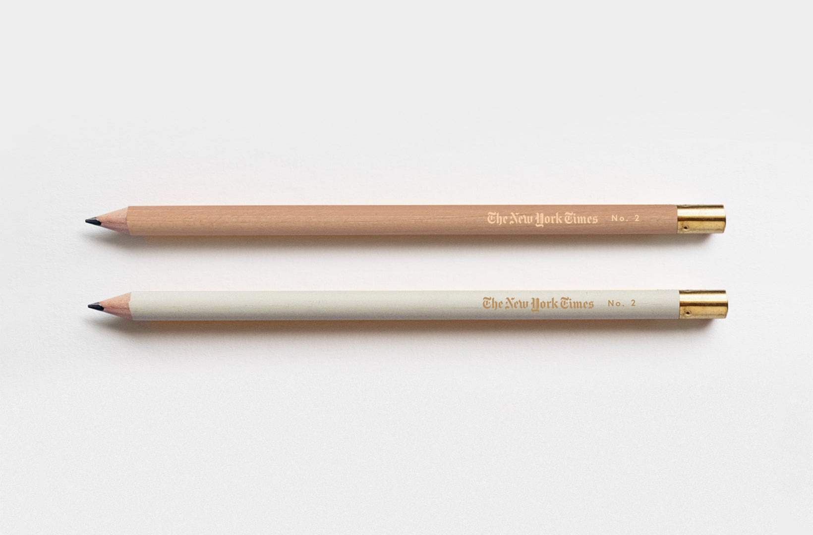 Two Appointed no. 2 pencils with gold foil custom logo sit against a beige background. one pencil is beige and one natural with gold foil caps