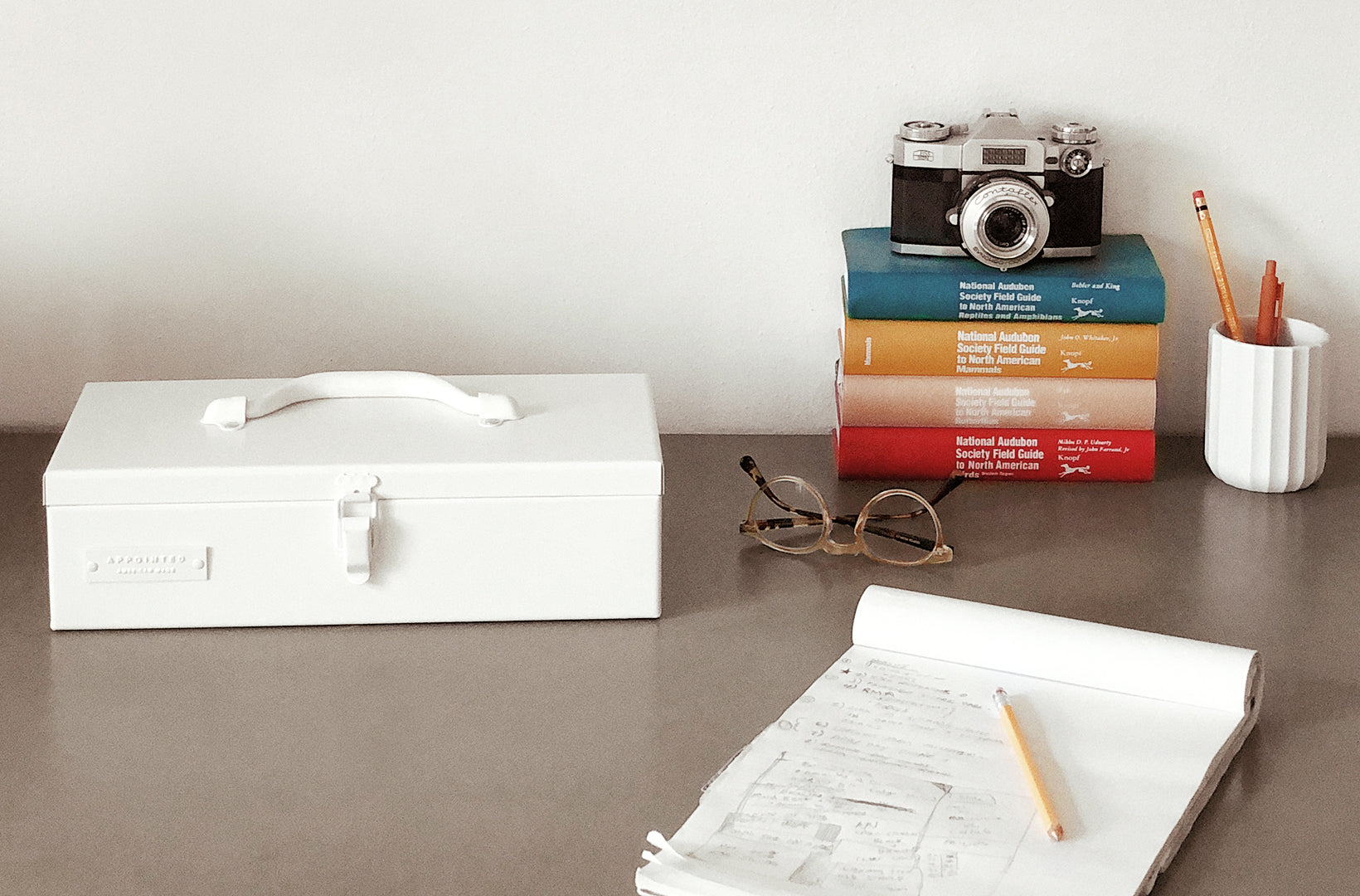 a porcelain colored toolkit sits on a gray desk with decorative accessories and a legal pad filled to the brim.