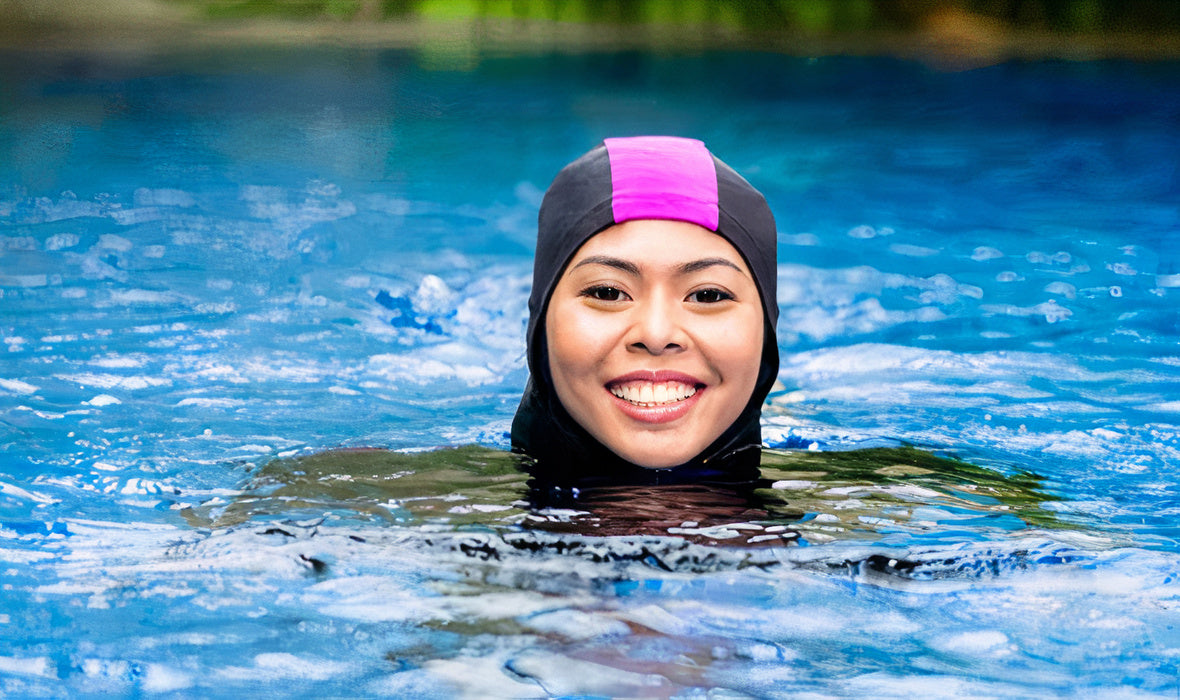 Une femme souriante, vêtue d'un burkini noir avec une bande rose sur la capuche