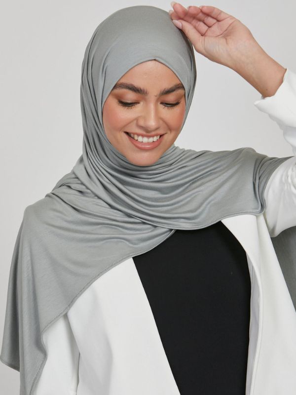 Une femme sourit et porte un hijab vert pierre