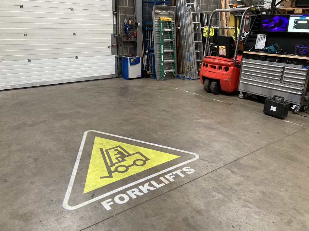Warehouse floor with white and yellow forklift truck warning sign projected onto it.