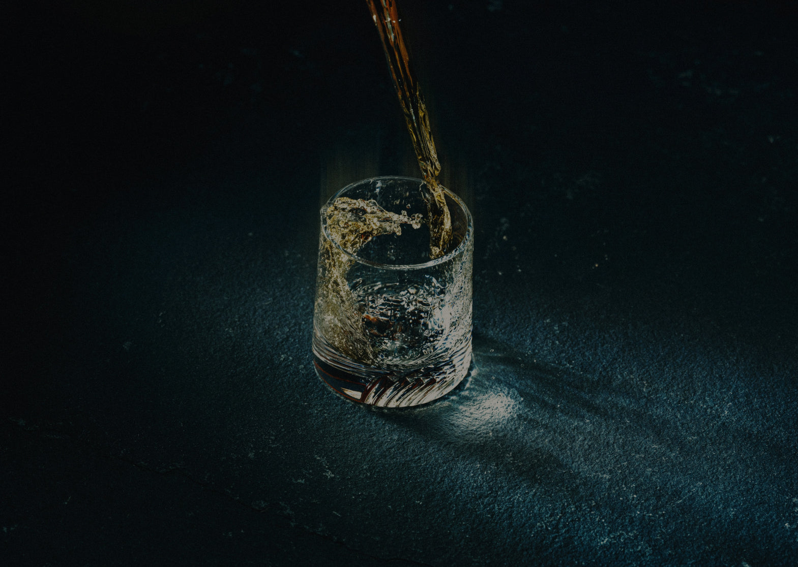 A drink being poured into a glass with splashes, set against a dark background.