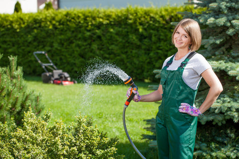 Donna con tubo da giardino che innaffia il suo prato in giardino