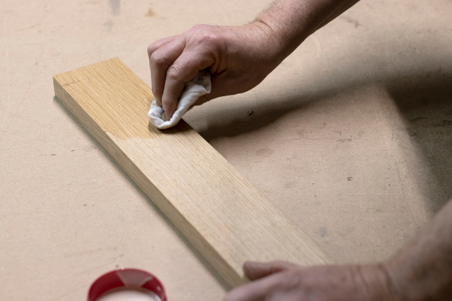 A man oiling a cut piece of oak using OSMO Polyox Oil Raw on a white cloth