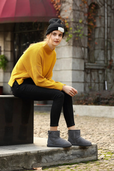 UGG Premium Mini Classic Suede Boots with a model sitting on a bench displaying the Grey Colour