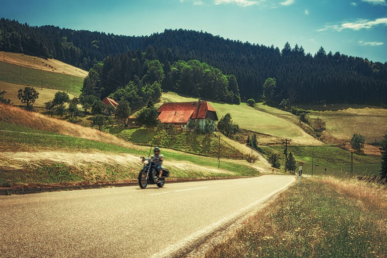 Biker driving along a country mountain road in autumn. Germany, Black Forest. Scenic countryside landscape with an old traditional house.