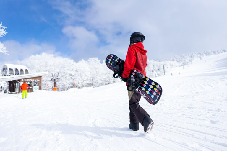 holding snowboard walking on snowy mountain