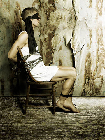 A man tied down to a chair with her ankles tied up.