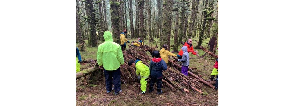Group learning survival skills = here they are learning to build a shelter in the wood using what's around