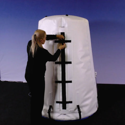 a woman latches the grand dive vertical hyperbaric chamber not pressurized in a blue room