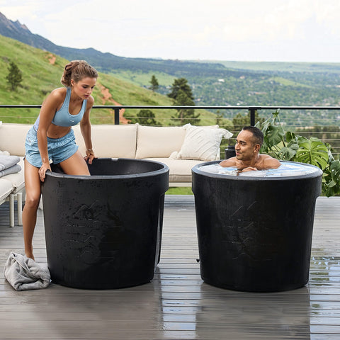 couple engages in cold plunge for health benefits. The ice baths sit on an outdoor deck with beautiful landscape behind them.