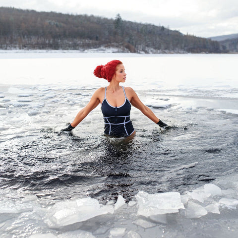 woman wades trough icy water in middle of a scenic winter landscape. She cold plunges for health benefits in natures ice bath