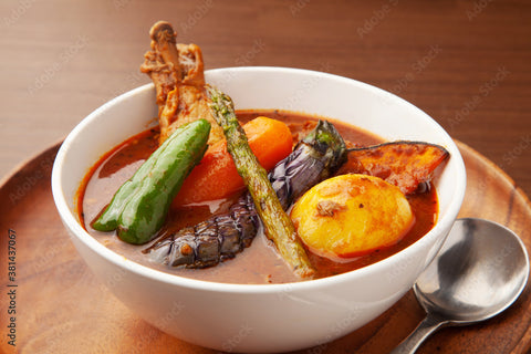 A bowl of Hokkaido soup curry with chicken and vegetables like okra, eggplant and more on top