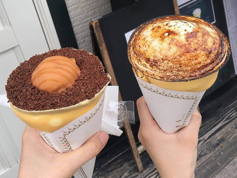 Two hands hold two crepes, one with chocolate and other with creme brulee