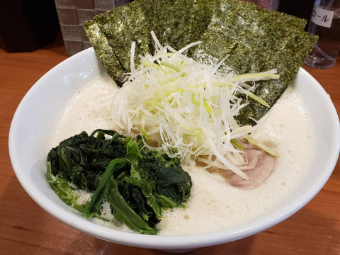 A bowl of creamy ramen with meat, seaweed and onion on top