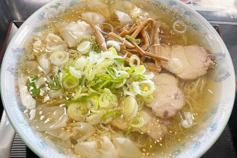 A bowl of Hokkaido's Kushiro Ramen sits on a table with wontons as a topping