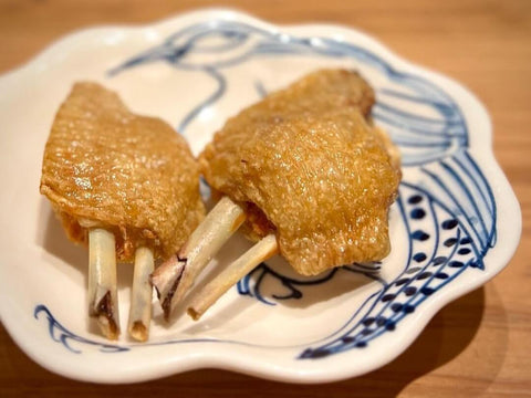 Two pieces of bone-in chicken sit on a plate in a kappo restaurant