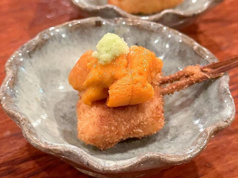 A single stick of kushikatsu with a sea urchin topping sits on a plate