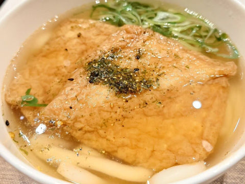 A bowl of kitsune udon with large fried tofu, green onion and seasoning on top