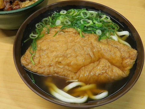 A bowl of kitsune udon with a large piece of fried tofu and plenty of green onion