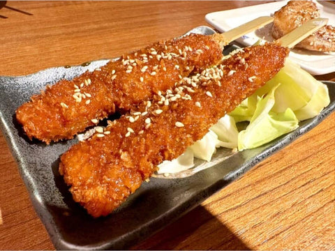 A plate of two meat kushikatsu coated in a light sauce over lettuce
