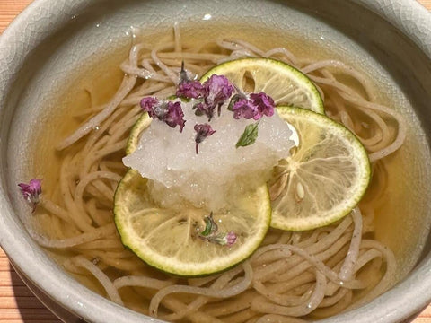 A bowl of soba with yuzu, daikon, and purple petals on top at a kappo restaurant