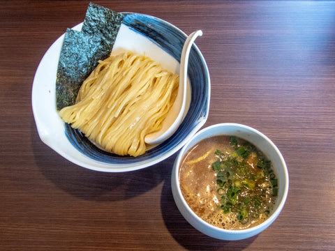A bowl of cold tsukemen ramen noodles sits next to a bowl of hot soup