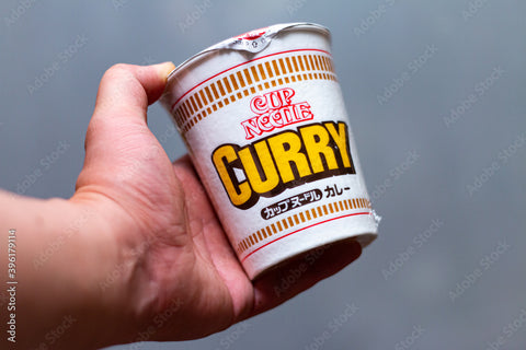 A hand holds a cup of Japanese curry noodles from Nissin