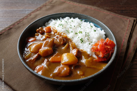 A bowl of Japanese curry with potato, carrot and beef alongside rice and red ginger